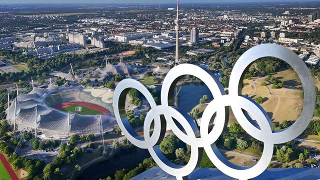 Luftaufnahme des Olympiaparks mit Olympiastadion, Olympia-Schwimmhalle und Olympiahalle, davor die Olympischen Ringe auf einer Dachkonstruktion (Fotomontage) 