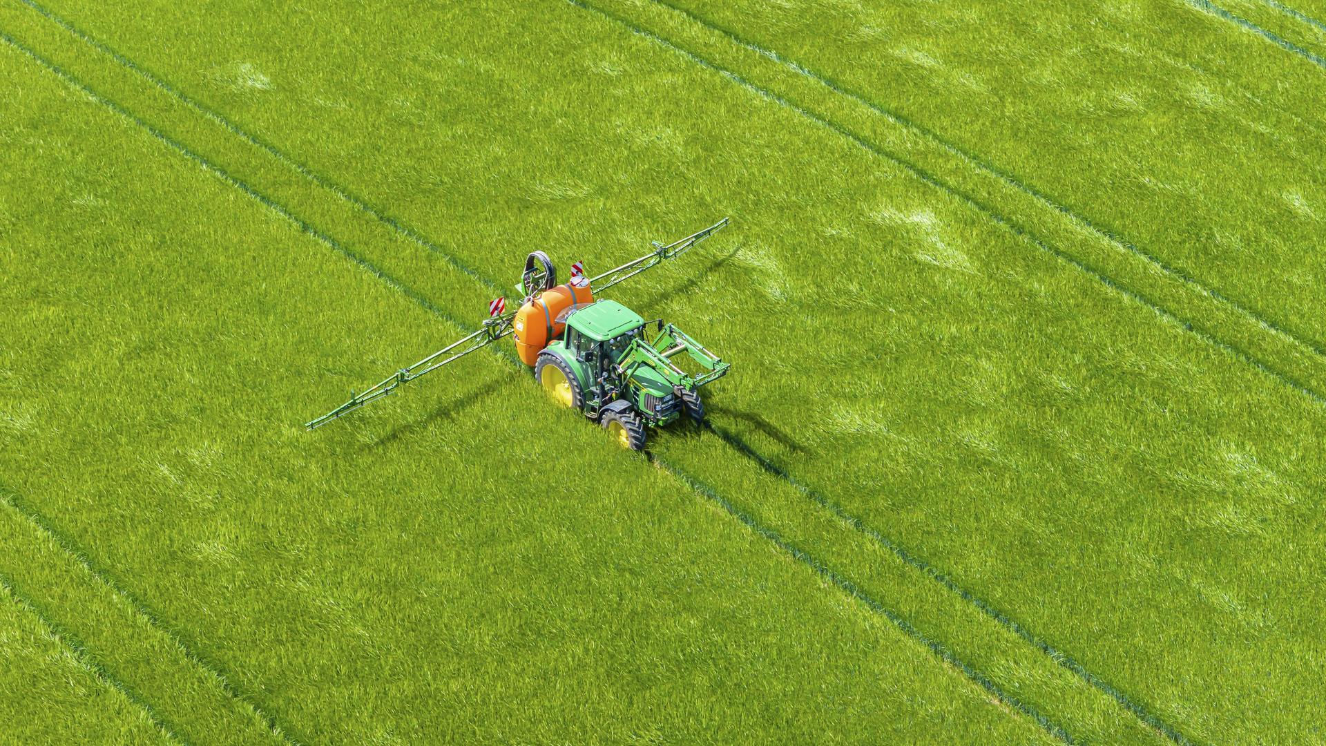 Das Drohnenfoto zeigt einen Traktor, der über eine Sprühvorrichtung mit zwei seitlichen Auslegern Flüssigkeit aus einem Tank auf einem Feld verteilt.