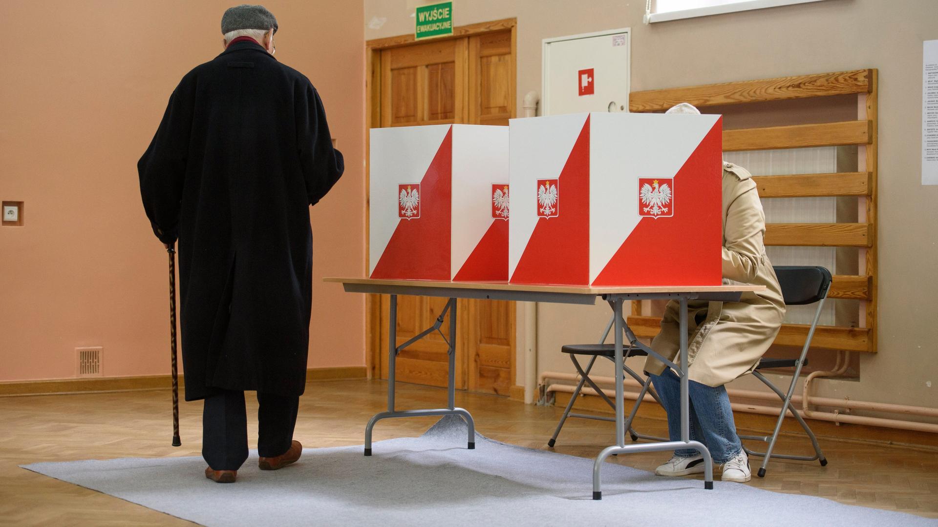 Ein Mann im schwarzen Mantel von hinten im Wahllokal in Warschau.