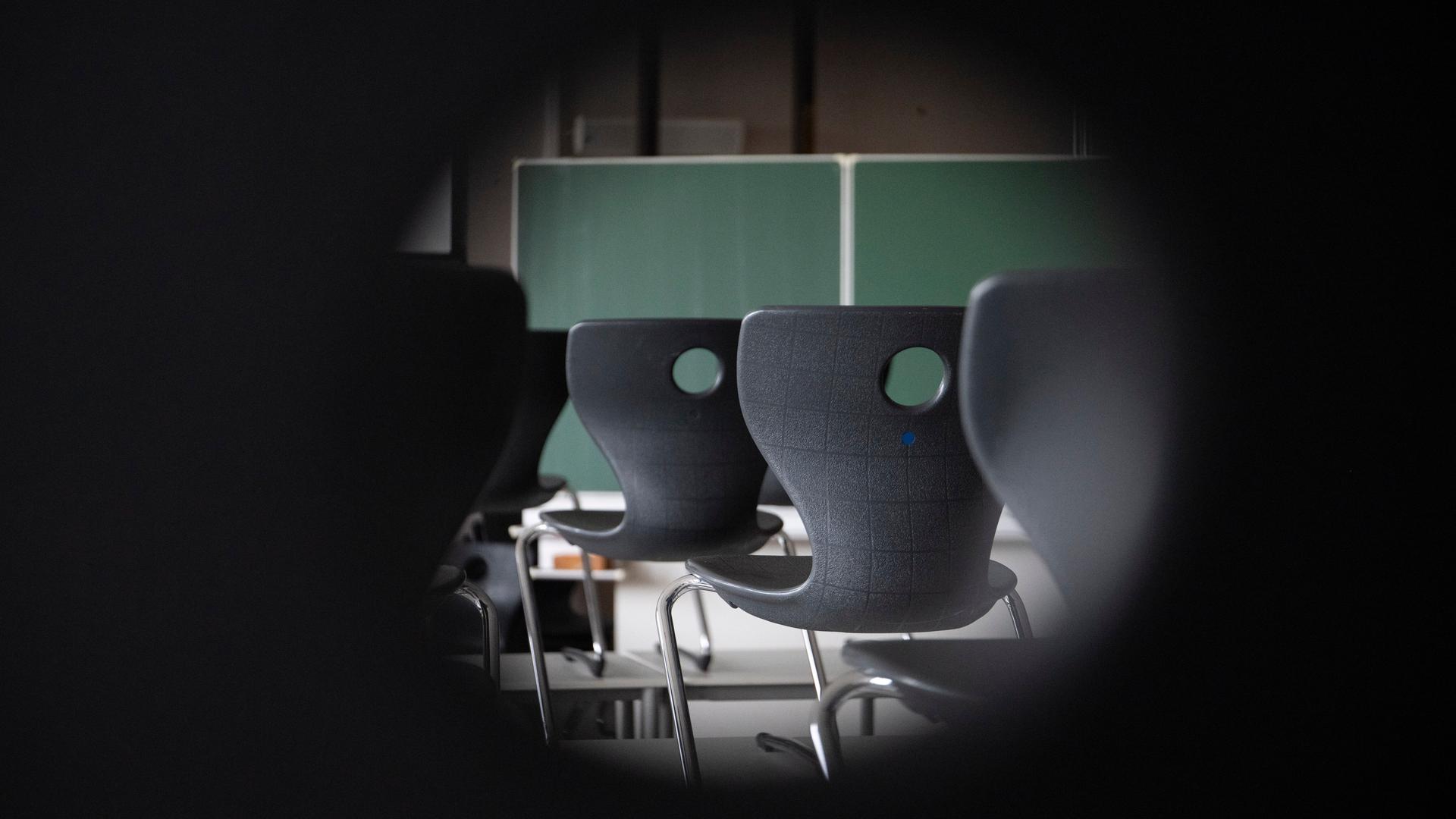 Blick durchs Schlüsseloch in ein Klassenzimmer. Zu sehen sind Stühle und eine Tafel.