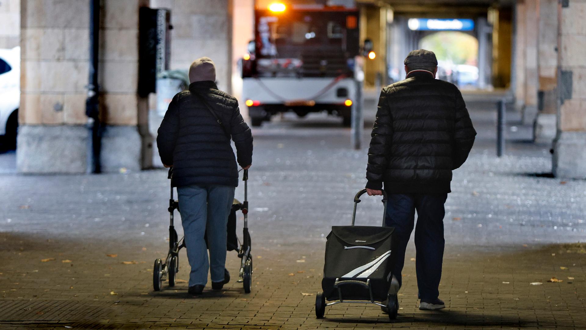 Rentnerpaar mit Rolator und Einkaufswagen in einer Unterführung im Halbdunkeln 