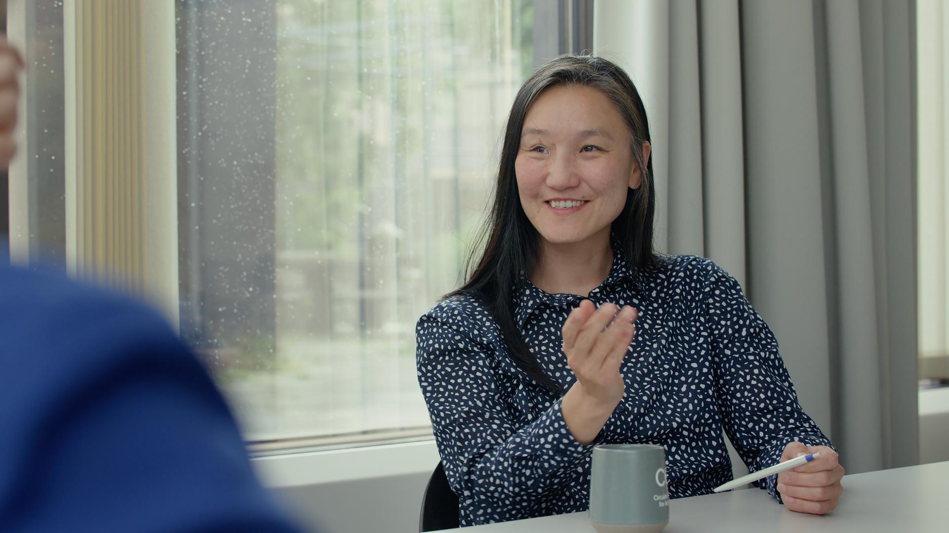 Saikal Zhunush sitzt an einem Tisch und spricht gestikulierend.