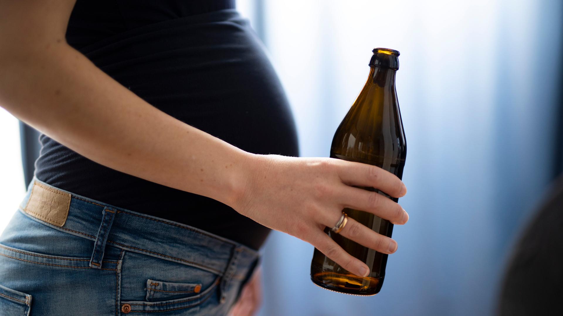 Seilticher Blick auf den Bauch einer schwangeren Frau, die eine Flasche Bier in der Hand hält