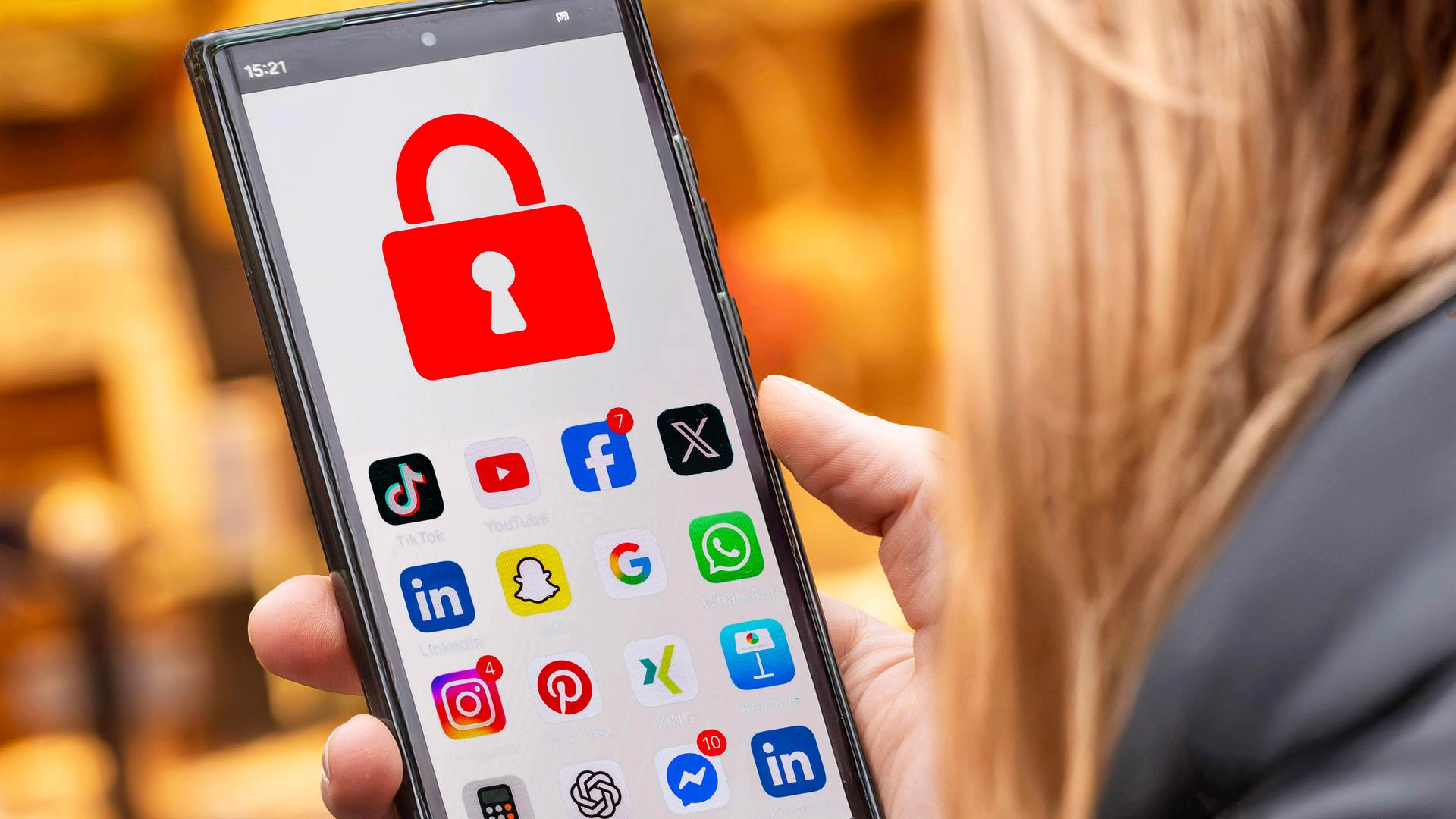 Symbolfoto: Schülerin mit Handy und Social Media Apps, die gesperrt sind