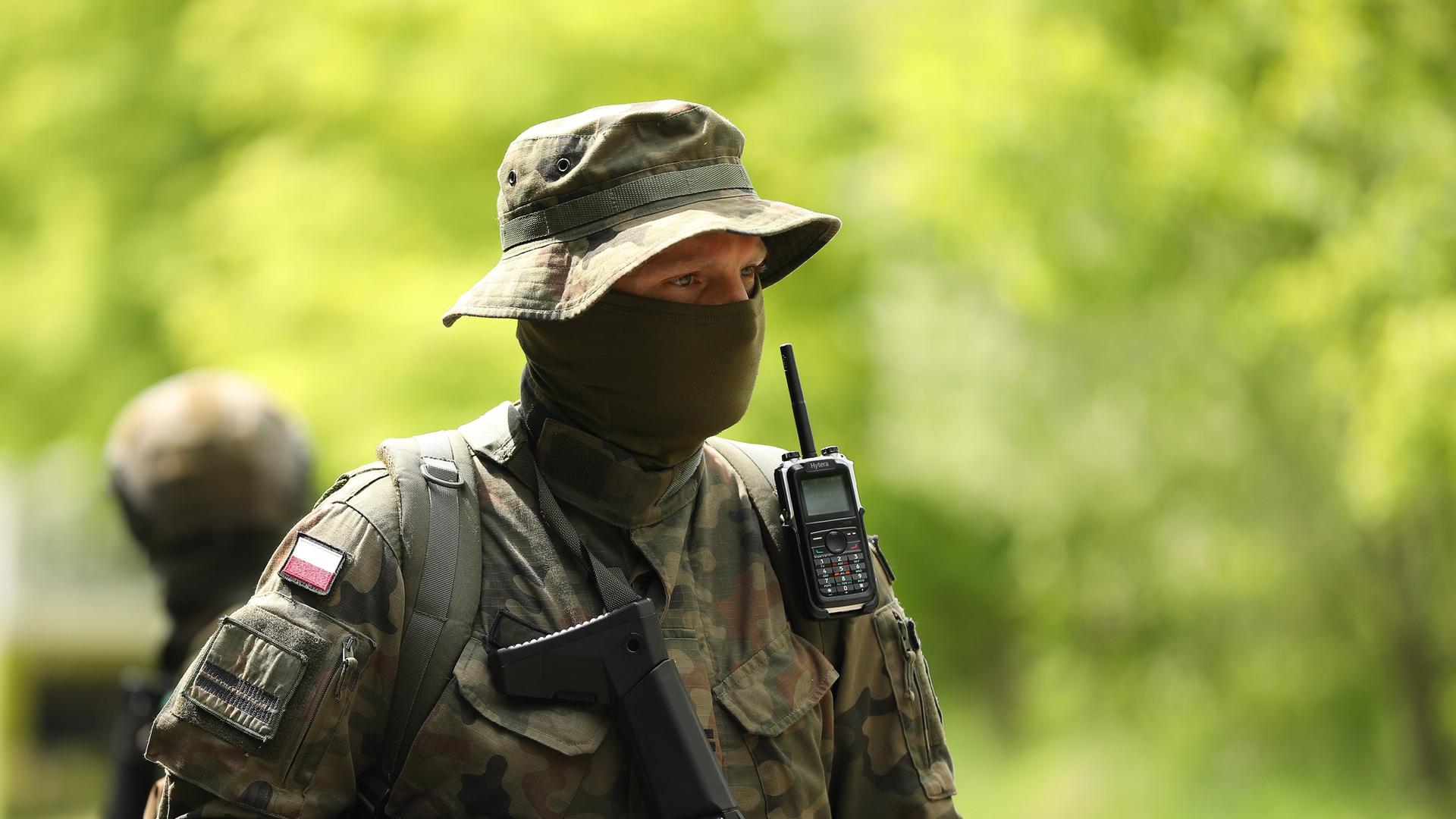 Ein vermummter polinischer Soldat trägt Uniform, Schlapphut und einen schwazren Schal vor seinem Gesicht