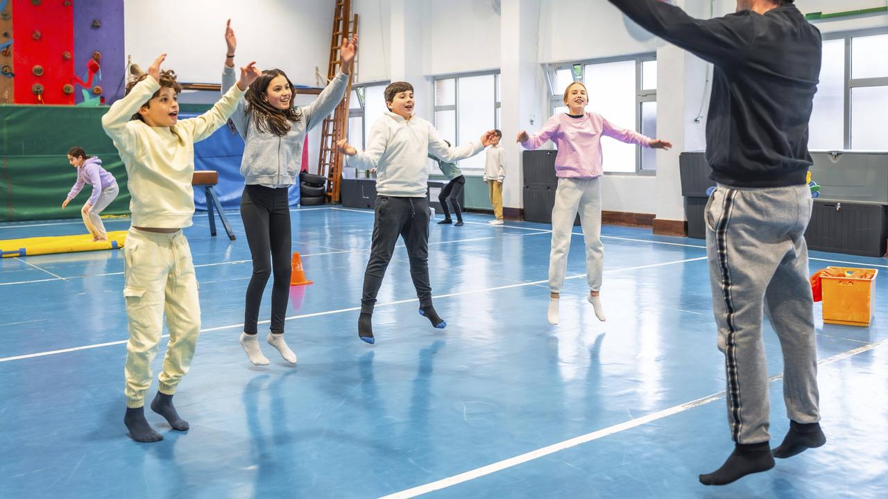 Symbolbild: Schüler machen zusammen mit ihrem Sportlehrer in der Schule Hampelmänner und Fitnessübungen.