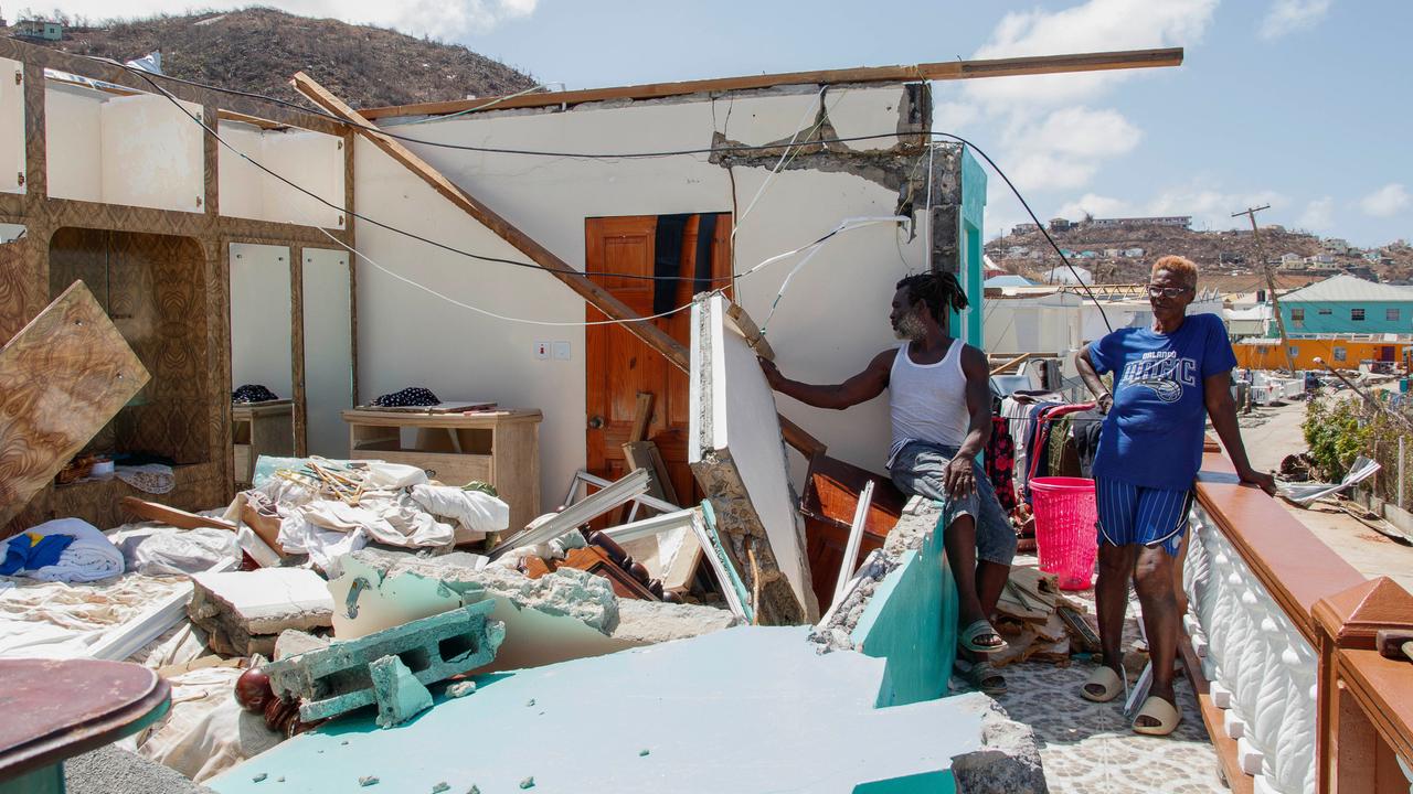 Zwei Menschen stehen neben einem zerstörten Haus.