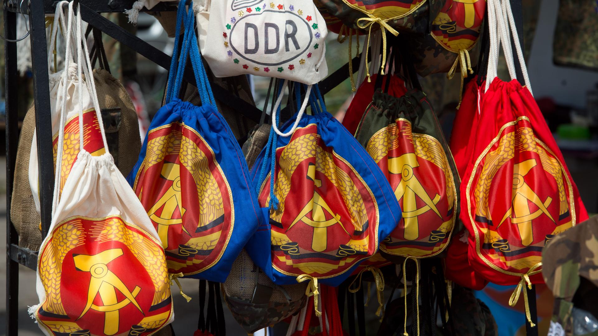 Taschen mit dem Staatswappen der DDR mit Hammer, Zirkel und Ährenkranz (hier nur als Kreis) werden an einem Stand verkauft.