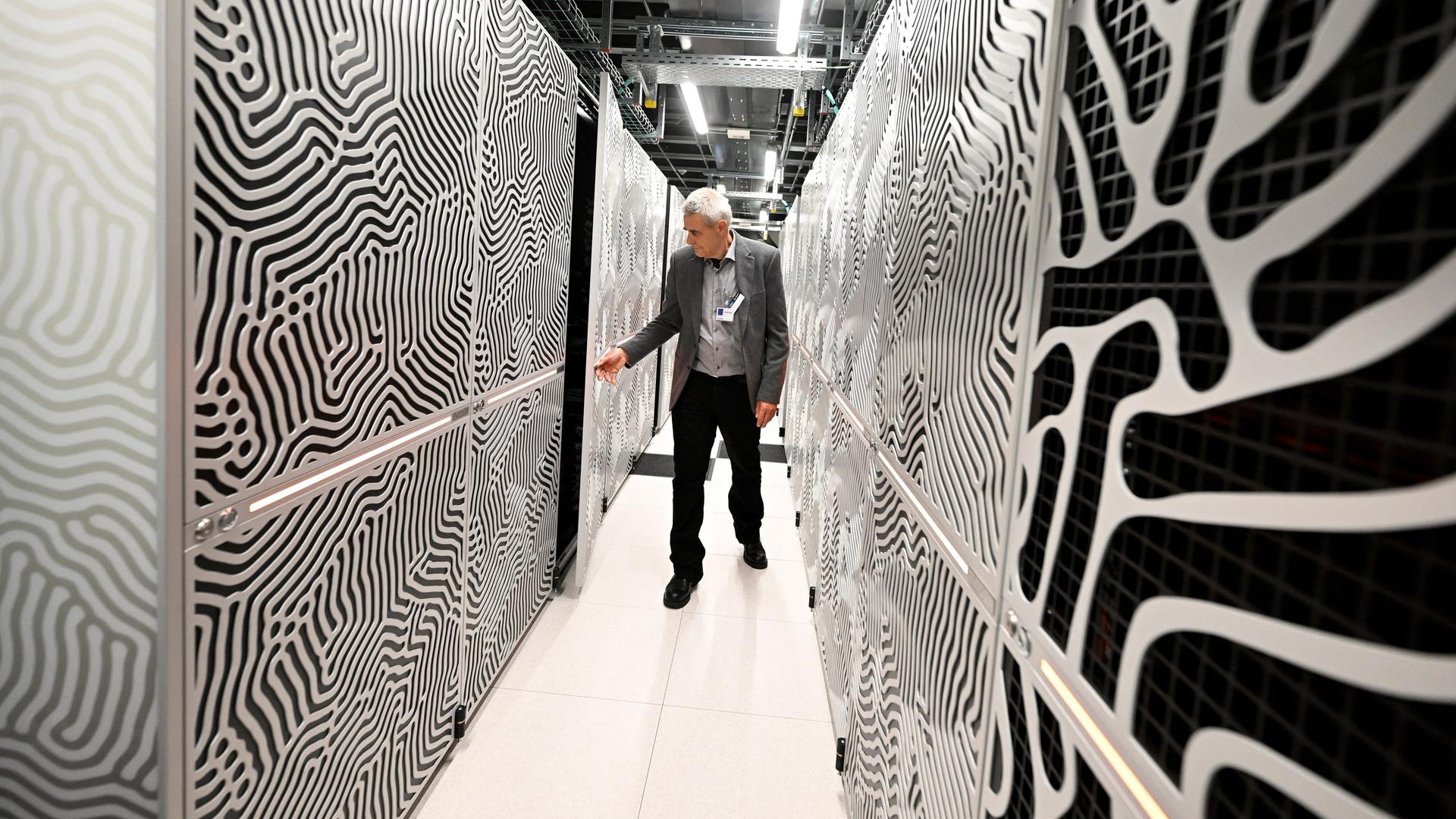 Ein Mitarbeiter steht in einem Flur zwischen den Servern des Supercomputers Jupiter.