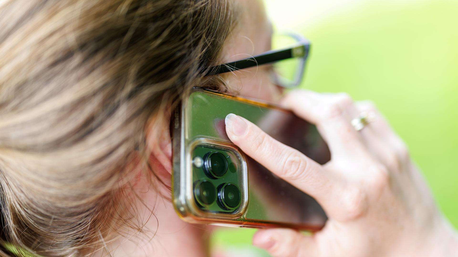 Eine junge Frau steht in einem Garten und telefoniert mit ihrem Smartphone.