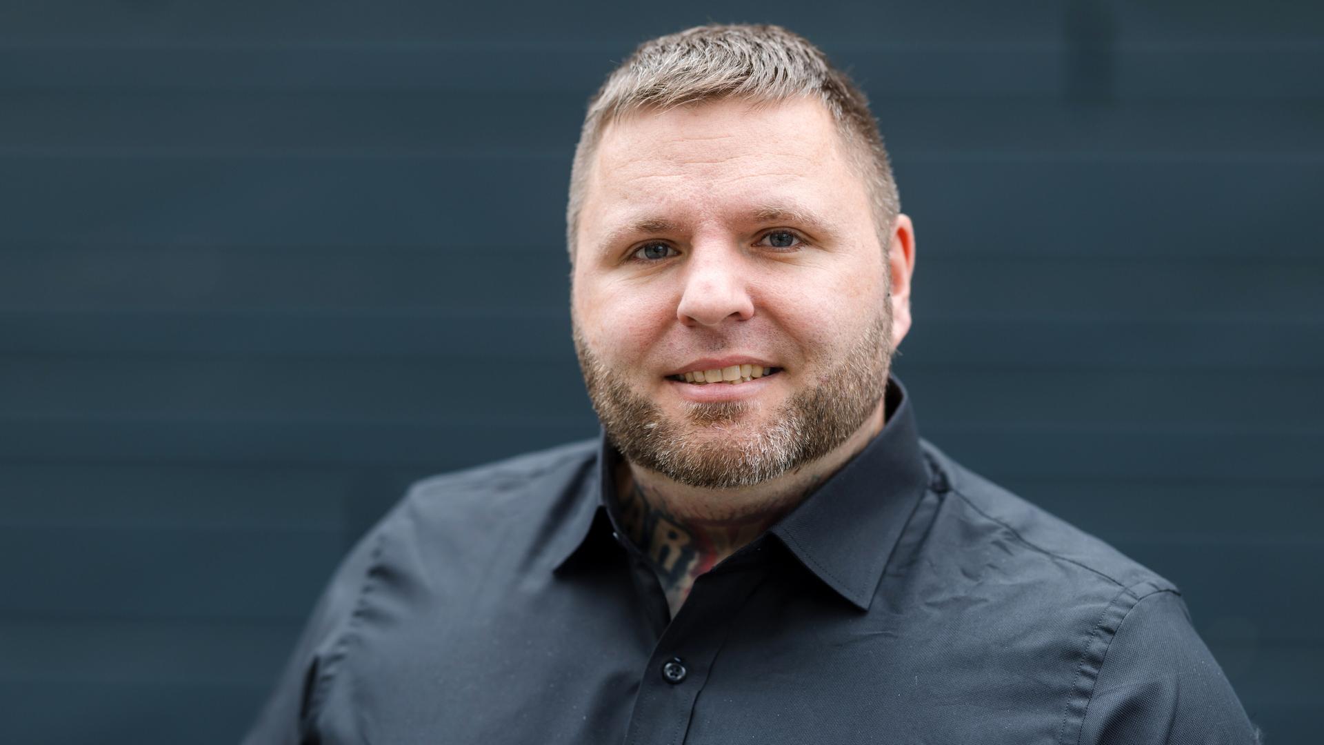 Tommy Frenck steht in schwarzem Hemd vor schwarzem Hintergrund und guckt in die Kamera.