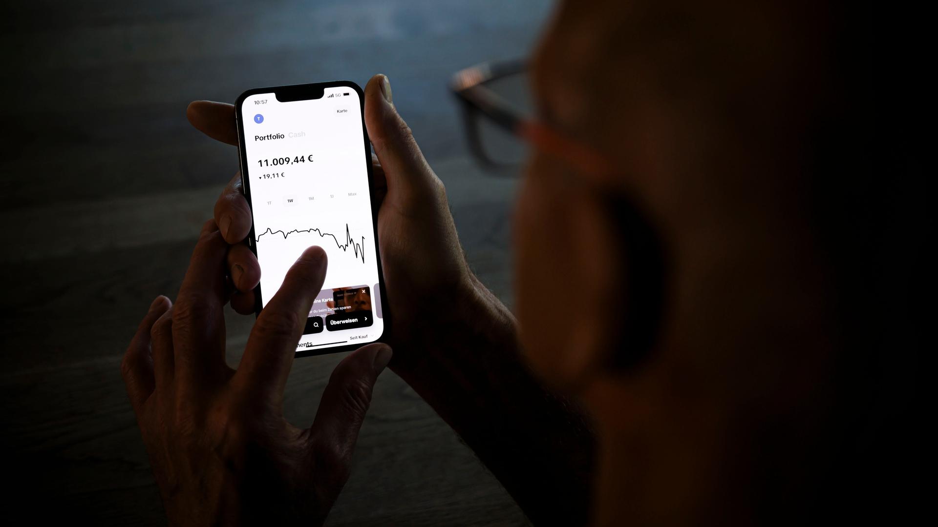 Ein Mann hält ein Smartphone mit einer geöffneten Trading-App und prüft den Aktienkurs seiner Geldanlage.