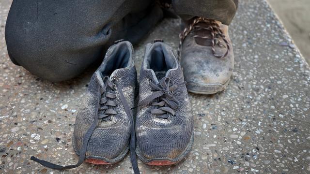 Ein Mann kniet hinter einem Paar Kinderschuhe.