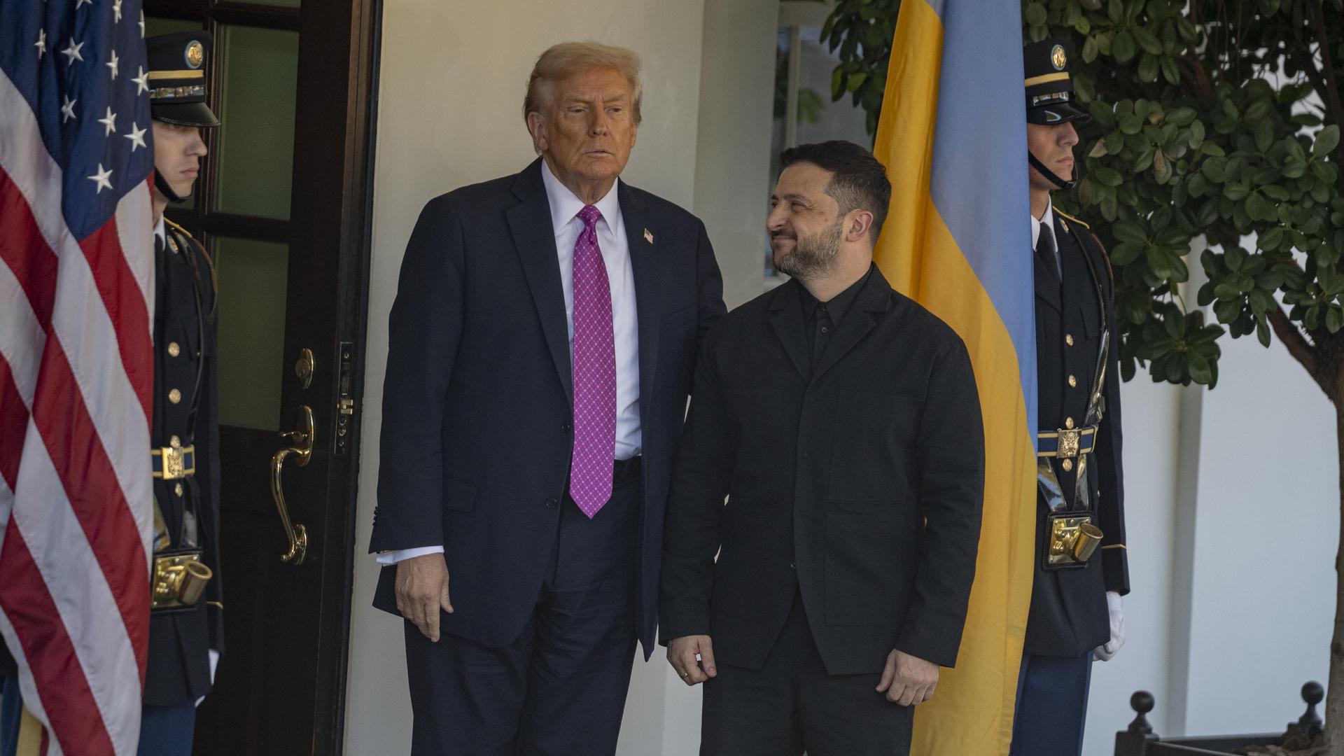 US-Präsident Donald Trump und der ukrainische Präsident Selenskyj stehen vor dem Weißen Haus. Selenskyi schaut zu Trump. Im Hintergrund sind US-Soldaten und die Landesfahne zu sehen.