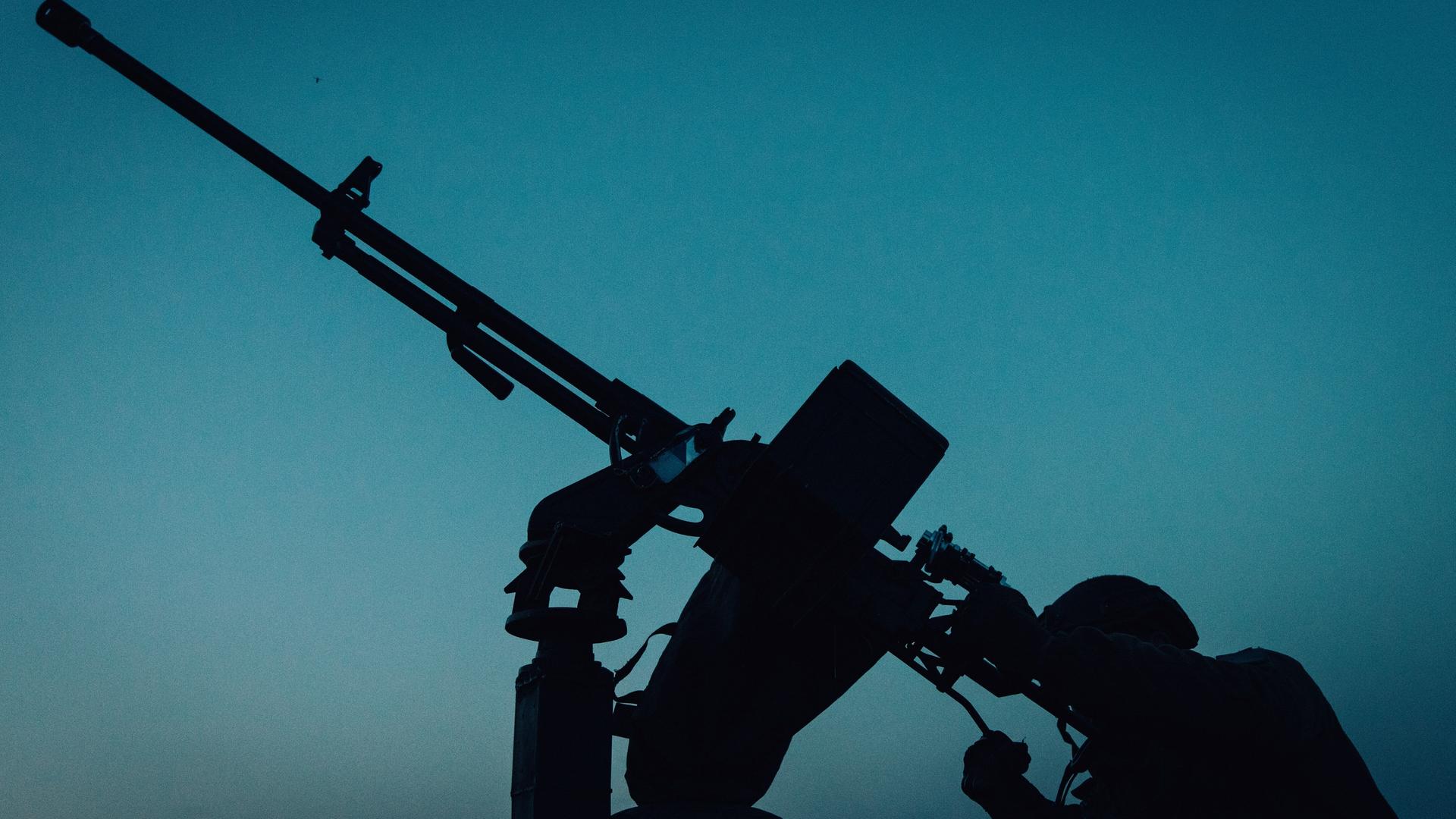 Ein ukrainischer Soldat sitzt vor einer mobilen Luftverteidiungsanlage und ist schemenhaft vor blauem Nachthimmel zu erkennen.
