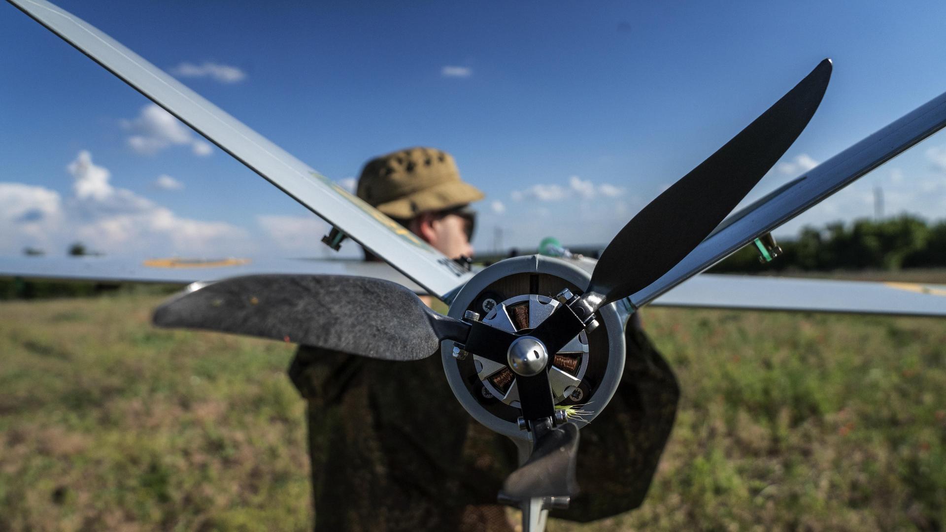 Ein Soldat steht auf einem Feld und hält eine Drohne in der Hand.