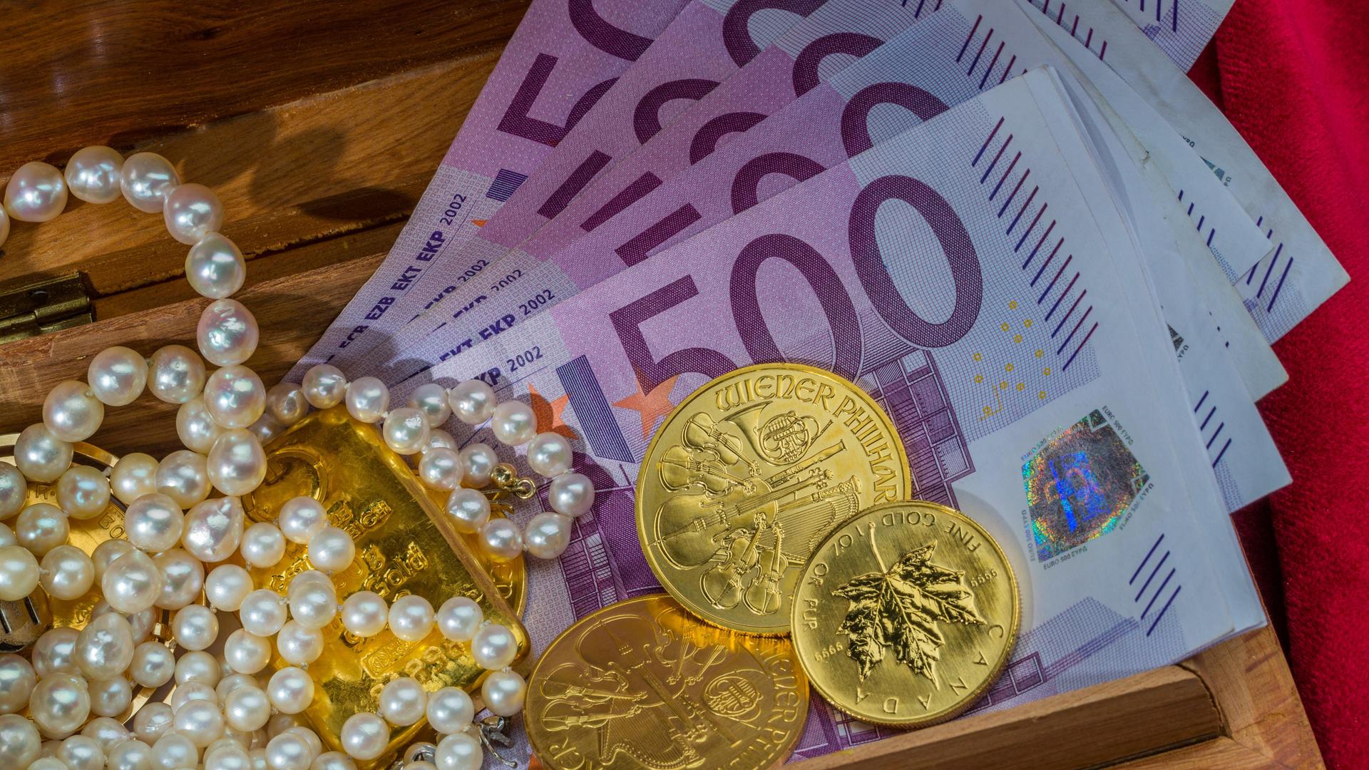 Gold in Münzen und Barren mit Schmuck auf rotem Samt. Symbolfoto für Reichtum