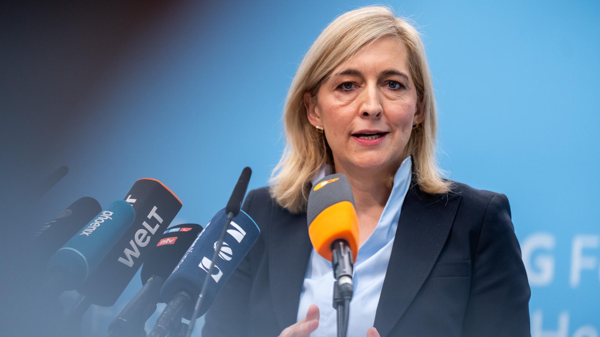 Nina Warken spricht bei einer Pressekonferenz zum geplanten Sparpaket gegen höhere Kassenbeiträge vor einem blauen Hintergrund in mehrer Mikrofone.
