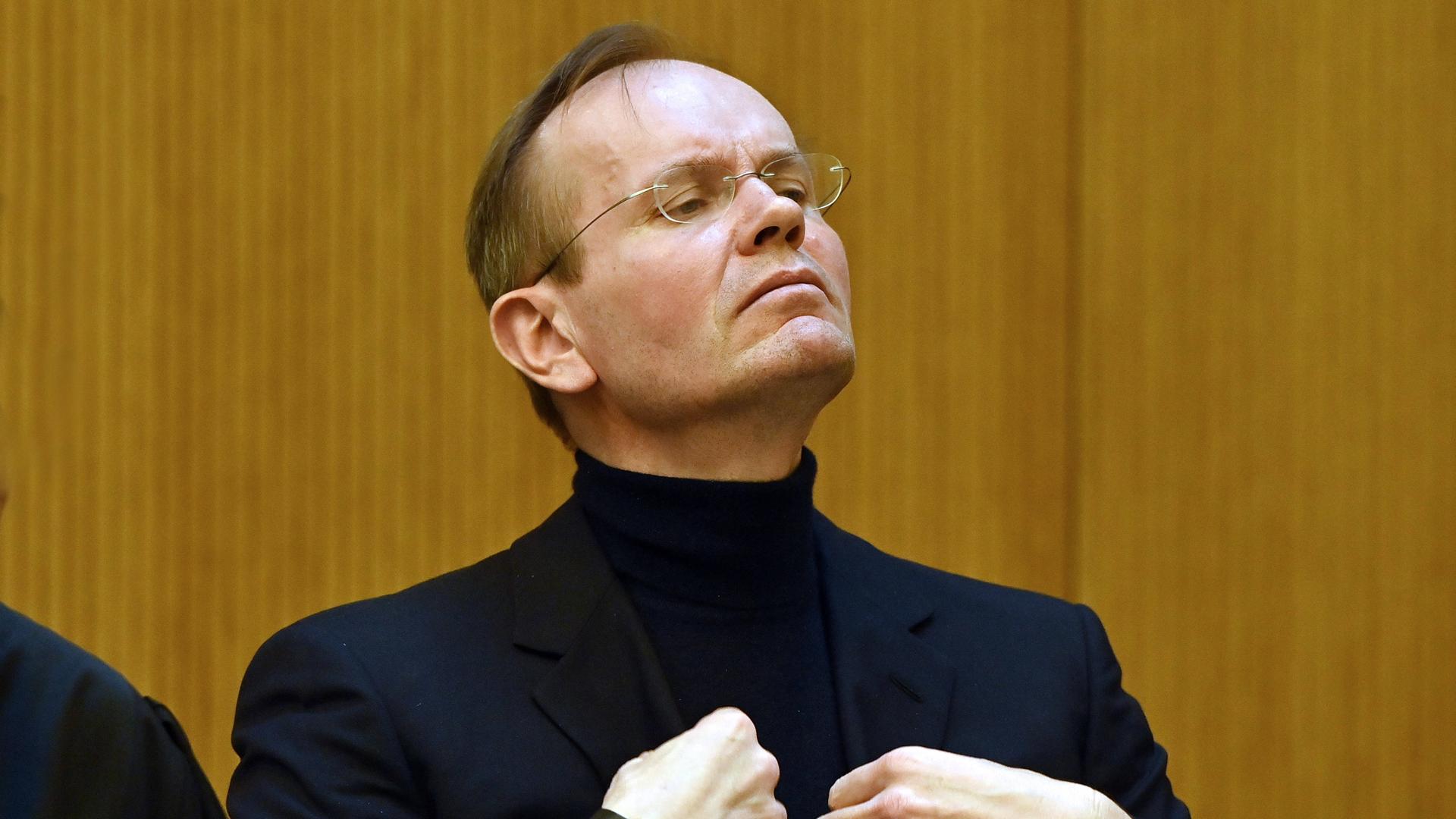 Markus Braun steht in einem schwarzen Anzug im Gerichtssaal und zupft sein Sakko zurecht.