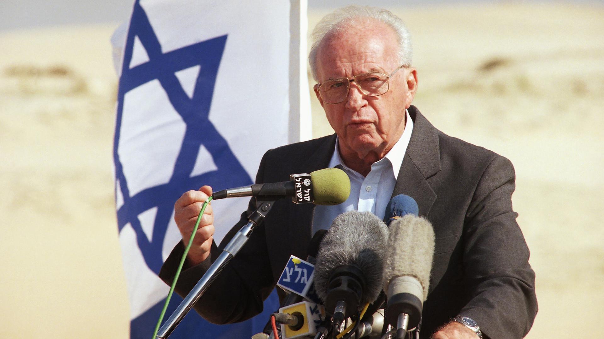 Israeli Prime Minister Yitzhak Rabin spricht 1994 vor einer israelischen Flagge in Mikrofone und hält eine geballte Faust hoch